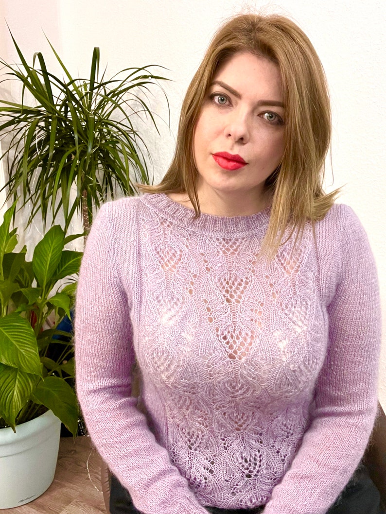 K&ouml;nnte beinhalten: Eine Frau tr&auml;gt einen helllila, durchbrochenen Strickpullover. Der Pullover hat ein zartes, durchbrochenes Design.
