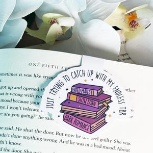 May include: A round bookmark with a purple, pink, and yellow illustration of a stack of books. The text on the bookmark reads "Just trying to catch up with my endless TBR".