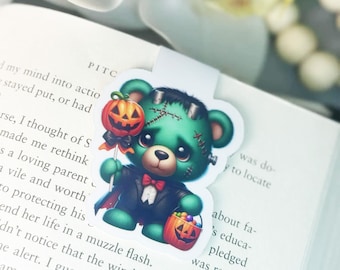 Könnte beinhalten: Ein grüner Teddybär, der sich für Halloween als Frankenstein verkleidet hat. Der Bär hält einen Lolli mit einer Kürbislaterne und einen Eimer Süßigkeiten mit einer Kürbislaterne.