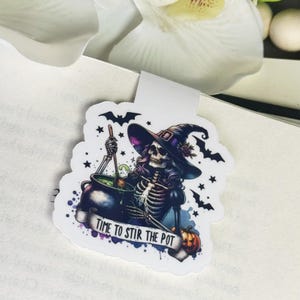 May include: A white sticker with a skeleton witch wearing a purple and black hat stirring a cauldron with a wooden spoon. The cauldron is filled with green liquid. The sticker has the text "Time to Stir the Pot" and stars and bats around the witch.