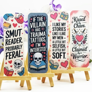 May include: Four decorative bookmarks with humorous text and illustrations. One reads "SMUT READER. PROBABLY FERAL." Another says "IF THE VILLAIN HAS TRAUMA TATTOOS, I'M INTERESTED." The third says "I LIKE MY STORIES LIKE I LIKE MY MEN - A LITTLE BIT SELFISH, A LITTLE BIT SOFT." The last says "Kissed by Chaos. Claimed by a Warrior."