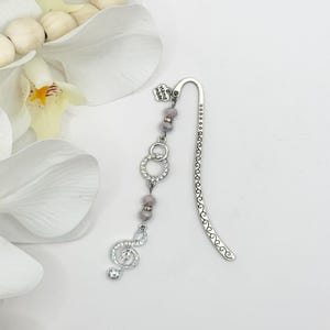 May include: Silver bookmark with a treble clef charm, silver beads, and a "hand made" tag. The bookmark is decorated with clear rhinestones.