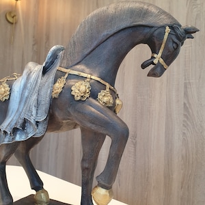 May include: A dark brown horse figurine with gold accents. The horse is wearing a decorative harness with gold flowers and is standing on a wooden base.