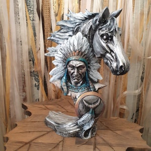Könnte beinhalten: Eine silberfarbene Figur eines Indianerhäuptlings mit Kopfbedeckung und Schild, hinter ihm ein Pferdekopf.
