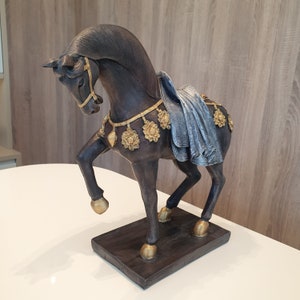 May include: A dark brown horse figurine with gold accents and a blue fabric saddle. The horse is standing on a dark brown base.