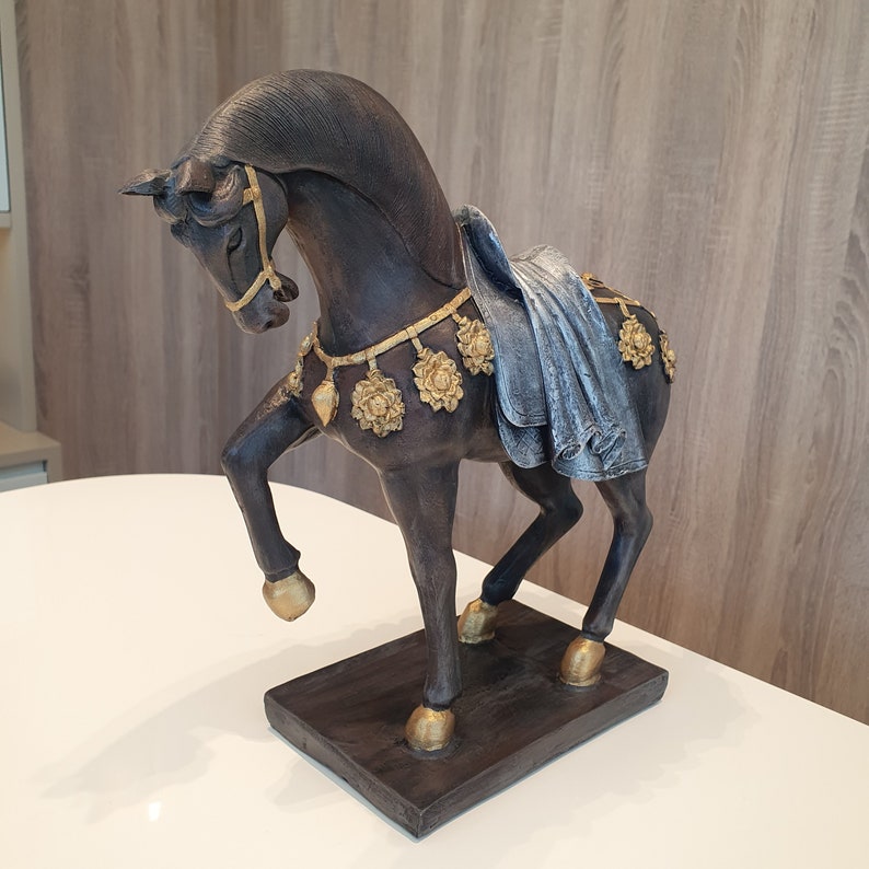 May include: A dark brown horse figurine with gold accents and a blue fabric saddle. The horse is standing on a dark brown base.