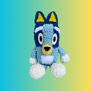 May include: A blue and white crocheted stuffed animal resembling a dog with yellow ears and a white patch on its chest.