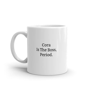 May include: White ceramic coffee mug with black text that reads "Cora Is The Boss, Period."
