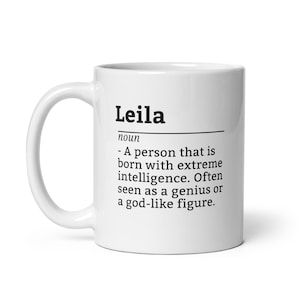 May include: White ceramic coffee mug with a black and white definition of the name "Leila" printed on it. The definition reads: "A person that is born with extreme intelligence. Often seen as a genius or a god-like figure."
