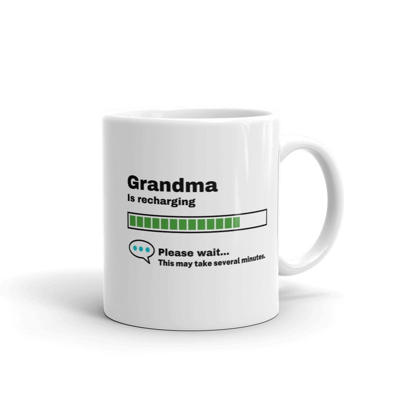 K&ouml;nnte beinhalten: Eine wei&szlig;e Keramik-Kaffeetasse mit einem schwarzen und gr&uuml;nen Design. Die Tasse sagt "Grandma is recharging" mit einem Fortschrittsbalken und dem Text "Please wait... This may take several minutes."