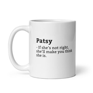 Op de afbeelding: Witte keramische mok met een zwarte tekstdefinitie van de naam "Patsy". De definitie luidt: "Als ze het niet bij het rechte eind heeft, zal ze je laten denken dat ze het wel heeft."