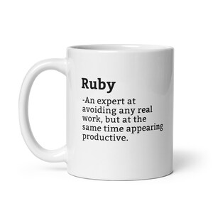 May include: White ceramic coffee mug with a black text design that reads "Ruby - An expert at avoiding any real work, but at the same time appearing productive."
