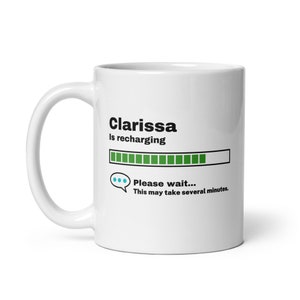 May include: White ceramic mug with a black graphic that says "Clarissa is recharging" with a green progress bar and the text "Please wait... This may take several minutes."