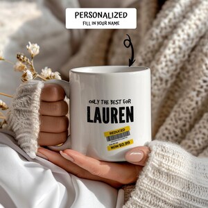 May include: White ceramic mug with the text "ONLY THE BEST FOR LAUREN" in black. A yellow "REDUCED" sticker is on the mug. The mug is held by a person wearing a cream-colored sweater. The top of the image reads "PERSONALIZED FILL IN YOUR NAME".