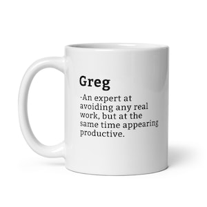 Könnte beinhalten: Eine weiße Keramiktasse mit einem schwarzen Textdesign, auf dem steht: "Greg - Ein Experte darin, jegliche wirkliche Arbeit zu vermeiden, aber gleichzeitig produktiv zu erscheinen."