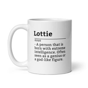 May include: White ceramic mug with the name "Lottie" printed in black, along with a definition describing a person with extreme intelligence. The mug has a curved handle and a glossy finish.