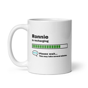 May include: White ceramic mug with a black graphic that says "Ronnie is recharging" with a green progress bar and the text "Please wait... This may take several minutes."