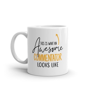 May include: White ceramic mug with a black and gold design. The mug features the text "THIS IS WHAT AN Awesome COMMENTATOR LOOKS LIKE" with an upward-pointing gold arrow. The mug has a white handle.