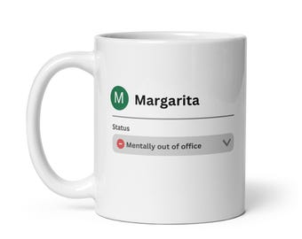 May include: White ceramic mug featuring the word "Margarita" and a green "M" icon. Below the text is a status bar that reads "Mentally out of office". The mug has a curved handle.