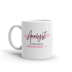 May include: White ceramic coffee mug with a pink brushstroke design and the text "Analyst in Progress" with a pink progress bar.