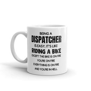 May include: White ceramic coffee mug with black text that reads "Being a Dispatcher is easy, it's like riding a bike except the bike is on fire, you're on fire, everything is on fire and you're in hell."
