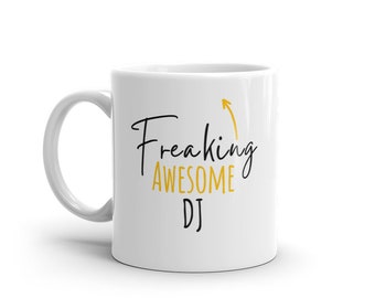 May include: White ceramic coffee mug with a black and gold design. The text on the mug reads "Freaking Awesome DJ" with an upward pointing arrow.
