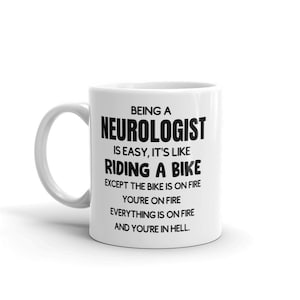 May include: White ceramic coffee mug with a black design that reads "Being a Neurologist is easy, it's like riding a bike except the bike is on fire, you're on fire, everything is on fire and you're in hell."