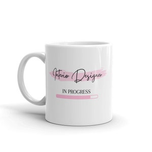 May include: White ceramic mug with a pink brushstroke design and the text "Interior Designer" in black cursive font. Below the text is a pink progress bar with the text "IN PROGRESS" in black.