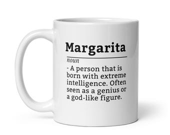 May include: White ceramic coffee mug with a black and white definition of the word "Margarita" as a noun. The definition reads: "A person that is born with extreme intelligence. Often seen as a genius or a god-like figure."