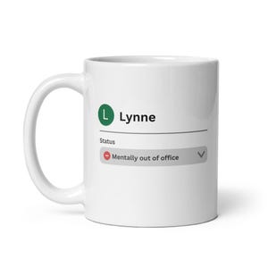 May include: White ceramic mug with the name "Lynne" and a green initial "L". The mug features a status indicator that reads "Mentally out of office". The mug has a curved handle.