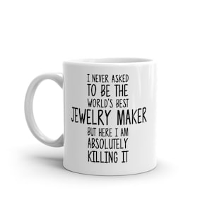 May include: White ceramic mug with a black handle. The mug features the text "I NEVER ASKED TO BE THE WORLD'S BEST JEWELRY MAKER BUT HERE I AM ABSOLUTELY KILLING IT" in black, bold font.