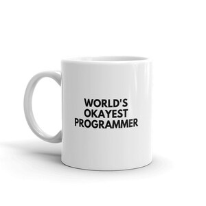 Puede incluir: Taza de cerámica blanca con texto negro que dice "WORLD'S OKAYEST PROGRAMMER".