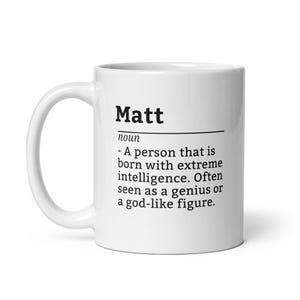 May include: White ceramic coffee mug with a black design that says "Matt noun - A person that is born with extreme intelligence. Often seen as a genius or a god-like figure."