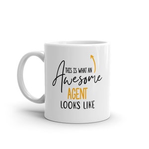 May include: White ceramic mug with the text "THIS IS WHAT AN Awesome AGENT LOOKS LIKE" in black and gold lettering. An upward-pointing gold arrow is next to the word "Awesome". The mug has a white handle.