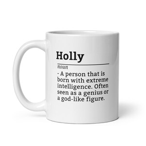 May include: White ceramic coffee mug with a black design that says "Holly noun - A person that is born with extreme intelligence. Often seen as a genius or a god-like figure."