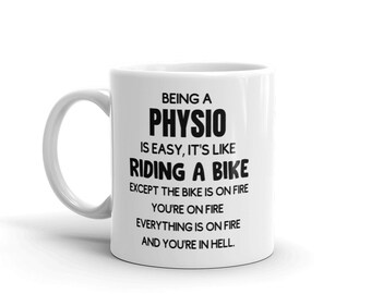 May include: White ceramic coffee mug with black text that reads "Being a Physio is easy, it's like riding a bike except the bike is on fire, you're on fire, everything is on fire and you're in hell."