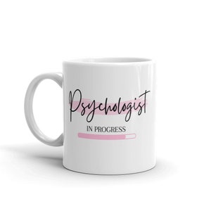 May include: White ceramic mug with a black and pink design. The mug says "Psychologist in progress" with a pink progress bar.