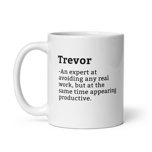 May include: White ceramic mug with the name "Trevor" printed in black, along with a humorous definition. The definition describes Trevor as an expert at avoiding work while appearing productive. The mug has a curved handle.