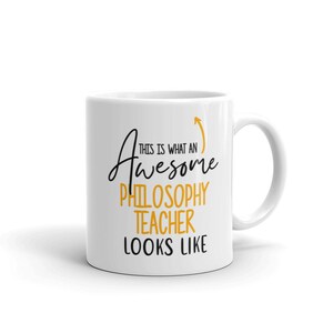 以下が含まれることがあります： 白のセラミックマグカップ。黒と金のテキストデザインで、「This is what an Awesome Philosophy Teacher Looks Like」と上向きの矢印が描かれています。 マグカップには湾曲したハンドルが付いています。