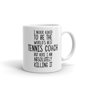 K&ouml;nnte beinhalten: Eine wei&szlig;e Keramik-Kaffeetasse mit schwarzem Text, der lautet: "Ich wurde nie gebeten, der beste Tennis-Trainer der Welt zu sein, aber hier bin ich und rocke es absolut."