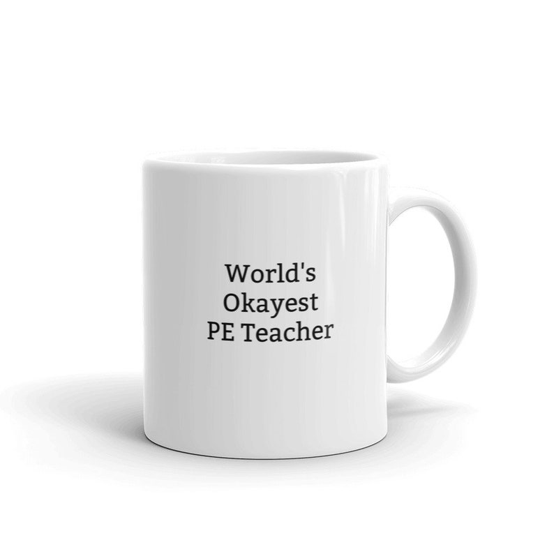 May include: White ceramic coffee mug with black text that reads "World's Okayest PE Teacher"