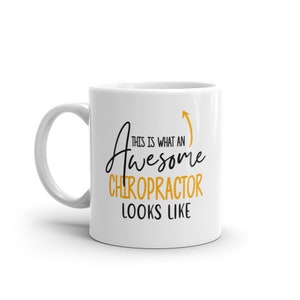 Może przedstawiać: Biały kubek ceramiczny z czarnym i złotym wzorem. Tekst na kubku brzmi "This is what an awesome chiropractor looks like".