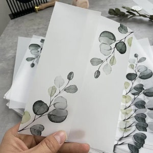 Puede incluir: Una pila de sobres blancos translúcidos con un diseño de hojas verdes en acuarela. Los sobres son perfectos para agregar un toque de elegancia a cualquier ocasión.
