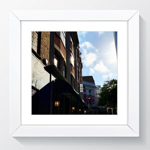 May include: A brick building with a blue awning and the word "IVVY" in white letters on the side. The building is in a city street with other buildings in the background. The sun is shining brightly in the sky.