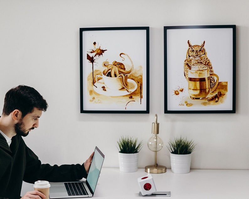 Puede incluir: Dos impresiones de arte de caf&eacute; enmarcadas en una pared blanca. La impresi&oacute;n de la izquierda presenta un pulpo en una taza de caf&eacute; con un dise&ntilde;o de mancha de caf&eacute;. La impresi&oacute;n de la derecha presenta un b&uacute;ho bebiendo caf&eacute; de una taza.