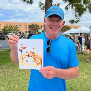 Puede incluir: Un hombre con una camisa azul y una gorra de b&eacute;isbol azul sostiene una tarjeta blanca con una ilustraci&oacute;n de acuarela de un pulpo en una taza de caf&eacute;. La ilustraci&oacute;n est&aacute; en tonos marrones y naranjas.