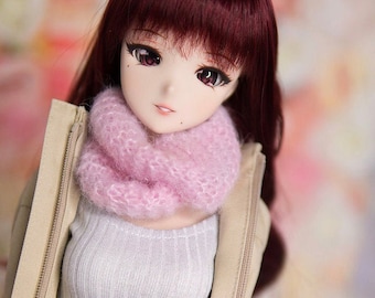 Peut inclure: Une poupée aux longs cheveux roux foncés portant une écharpe en tricot rose, un pull blanc, une veste beige et un jean bleu.