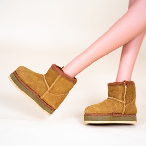 May include: A pair of brown suede ankle boots with a green trim around the sole.