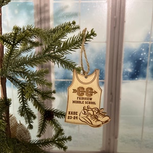 May include: A wooden ornament shaped like a running singlet with the text "CC Fairview Middle School Kade 23-24" and a pair of running shoes.