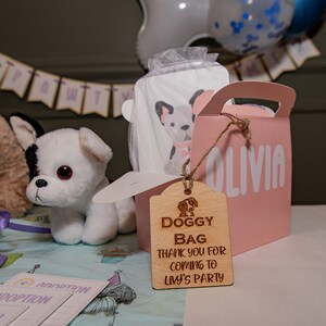 Peut inclure: Sc&egrave;ne de f&ecirc;te avec un jouet en peluche chien blanc et noir, un sac cadeau rose avec "OLIVIA" imprim&eacute; dessus, et une &eacute;tiquette en bois avec "DOGGY BAG THANK YOU FOR COMING TO LIV'S PARTY". Des cartes sur le th&egrave;me de l'adoption sont &eacute;galement pr&eacute;sentes.